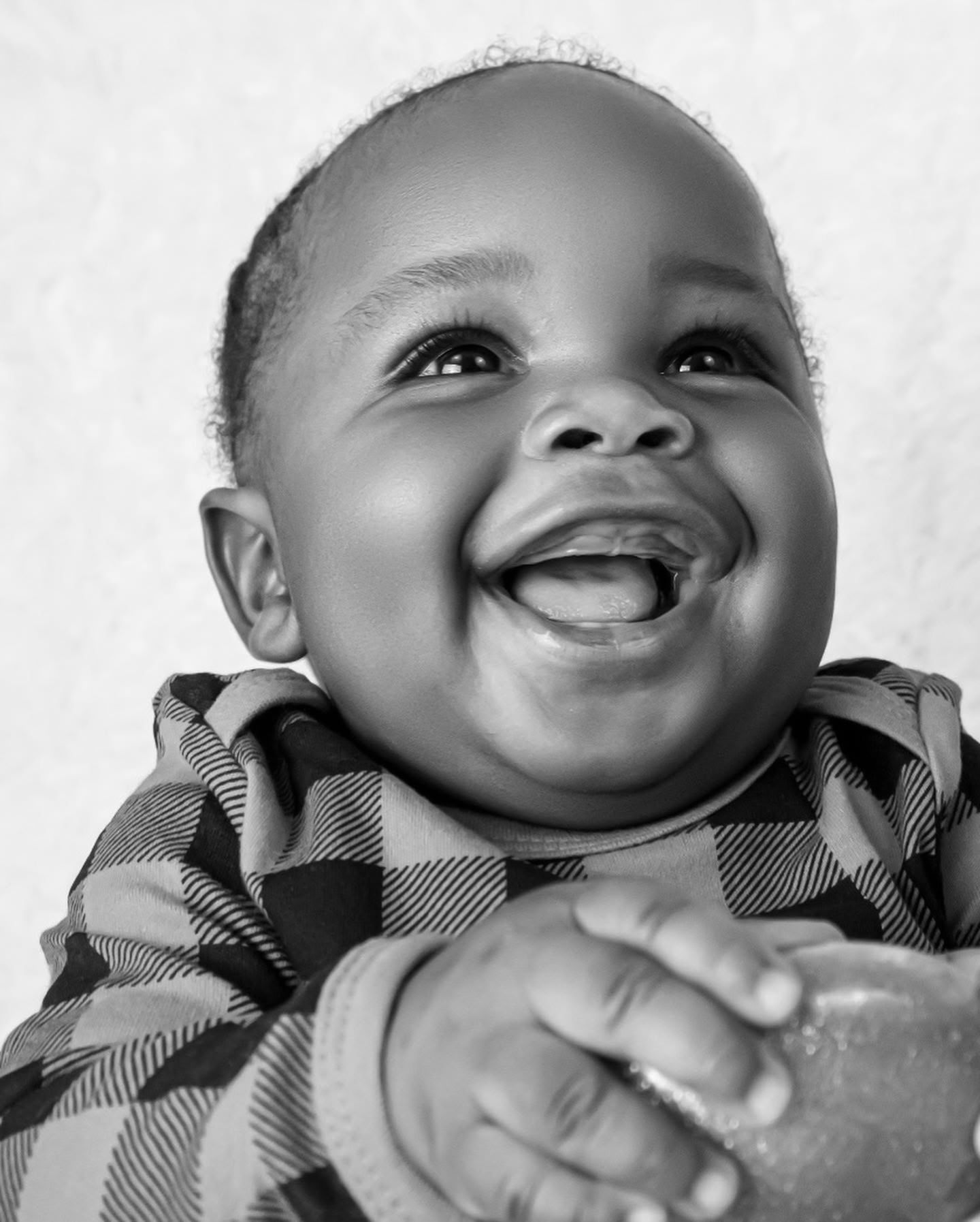 Baby wearing plaid outfit smiling and laughing in black and white portrait series.