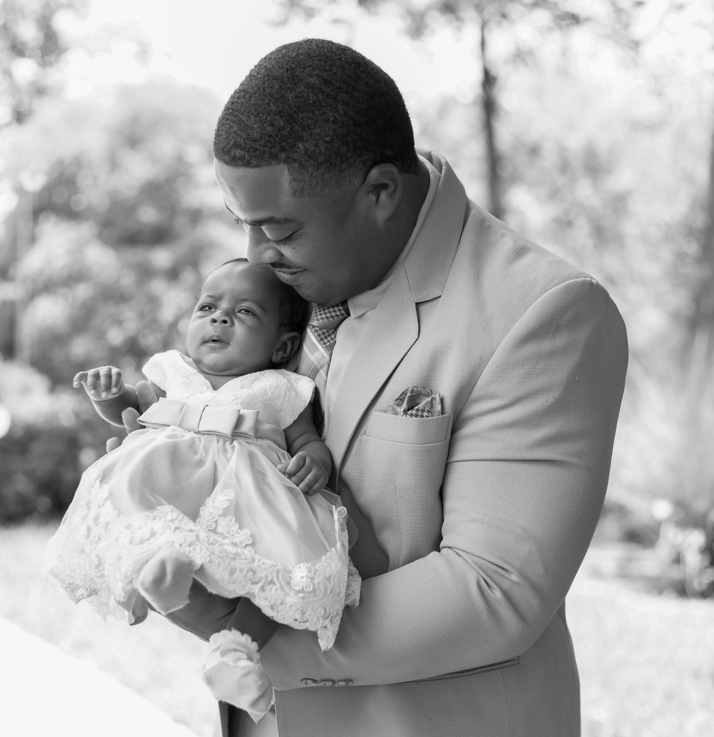 A tender black and white photo series showing an intimate moment between parent and infant in formal attire.