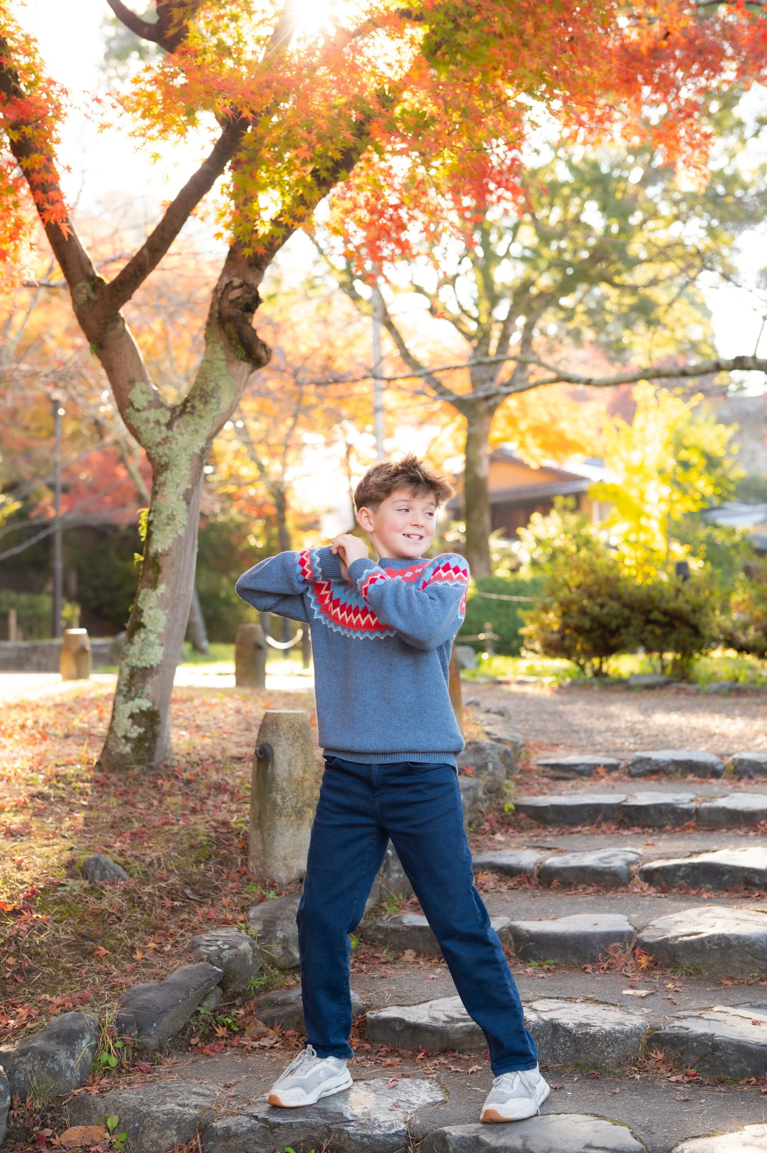 A young boy poses playfully on stone steps in a park with bright autumn maple trees.