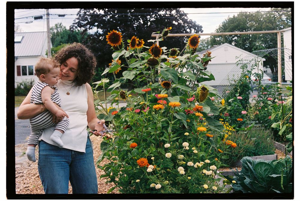 Mother holds daughter next to homegrown flower garden during a family session at their home in August in Biddeford, Maine.