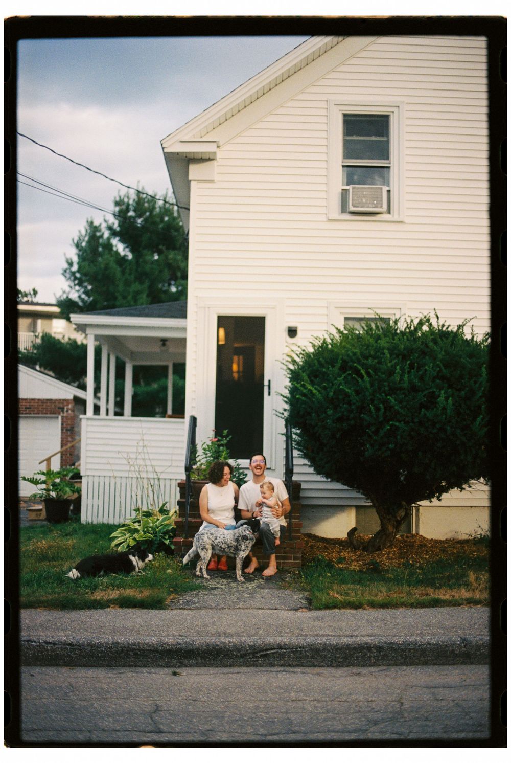 Family portrait at home in Biddeford, Maine with two cattle dogs in the front yard on the front steps of their first home with first child