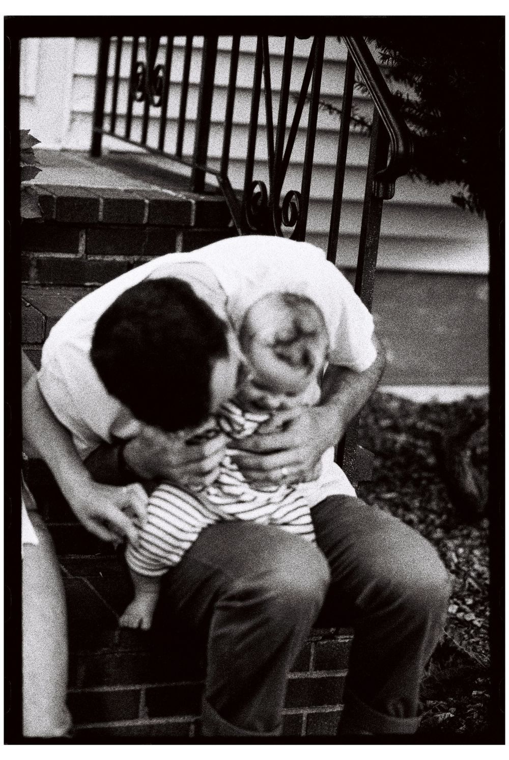 Black and white 35mm film photograph of a father holding his daughter and making her laugh on his knee outside their home in southern Maine.