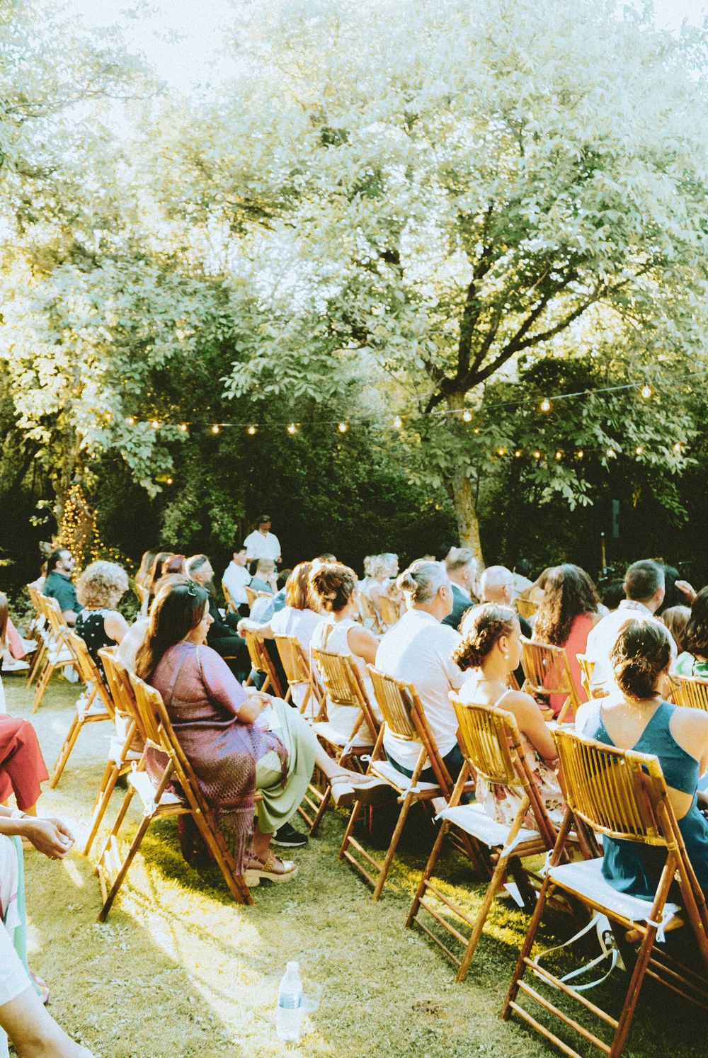 Outdoor wedding ceremony in a garden setting with guests seated under natural light.