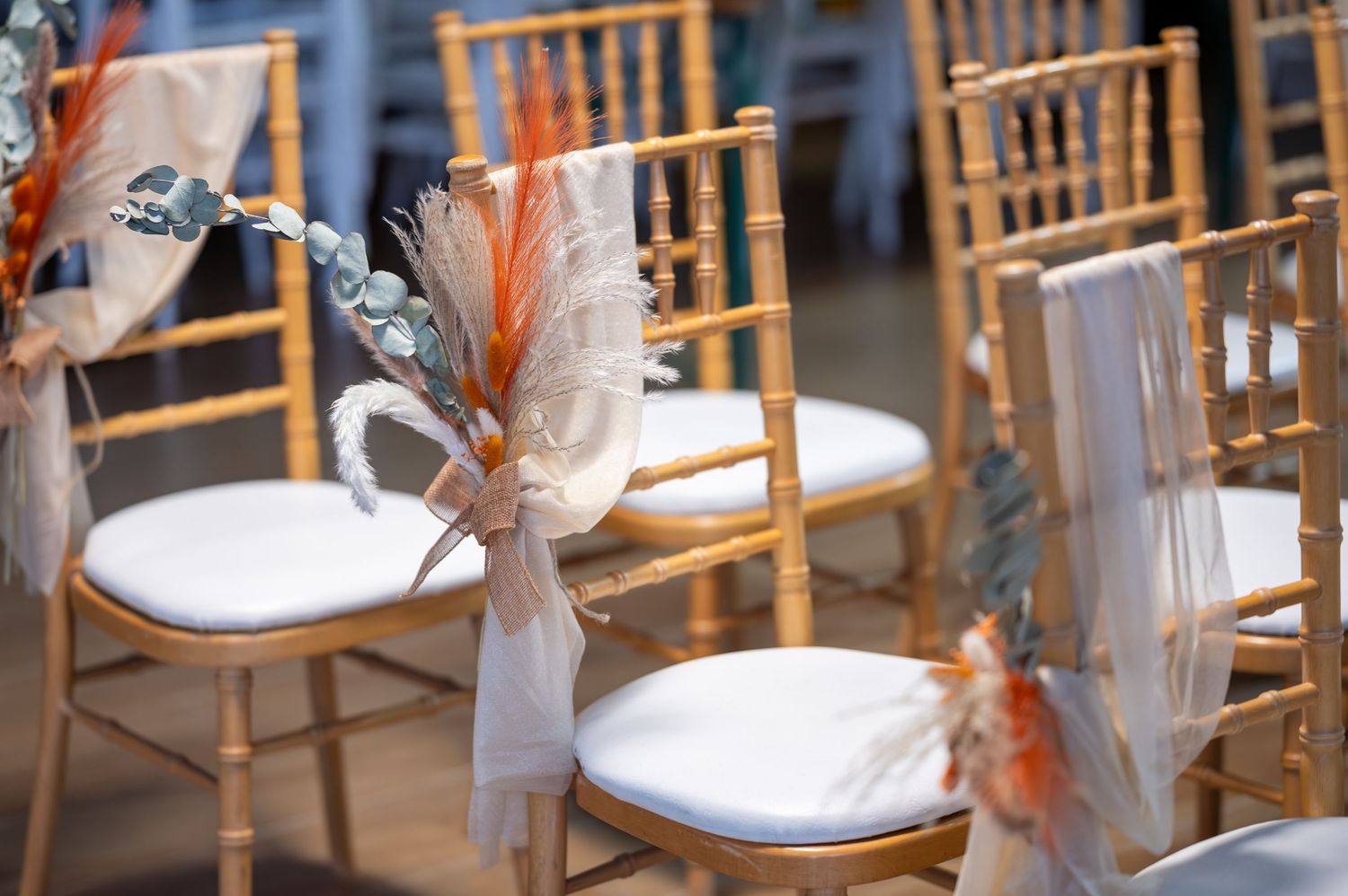 Des chaises Chiavari dorées avec des coussins blancs s'alignent dans un élégant lieu de réception de mariage.