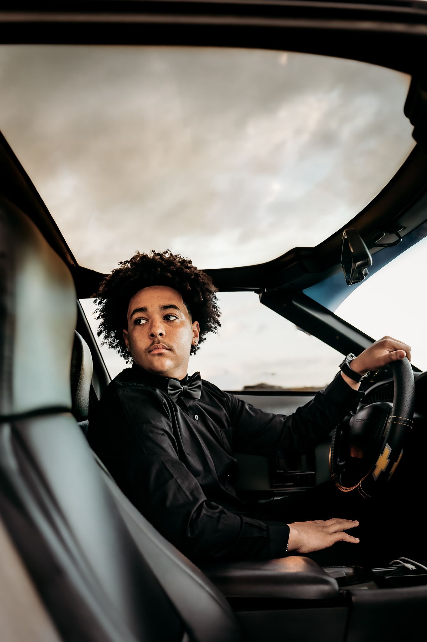 Young Senior Male in a car dressed in all black looking behind him very seriously.