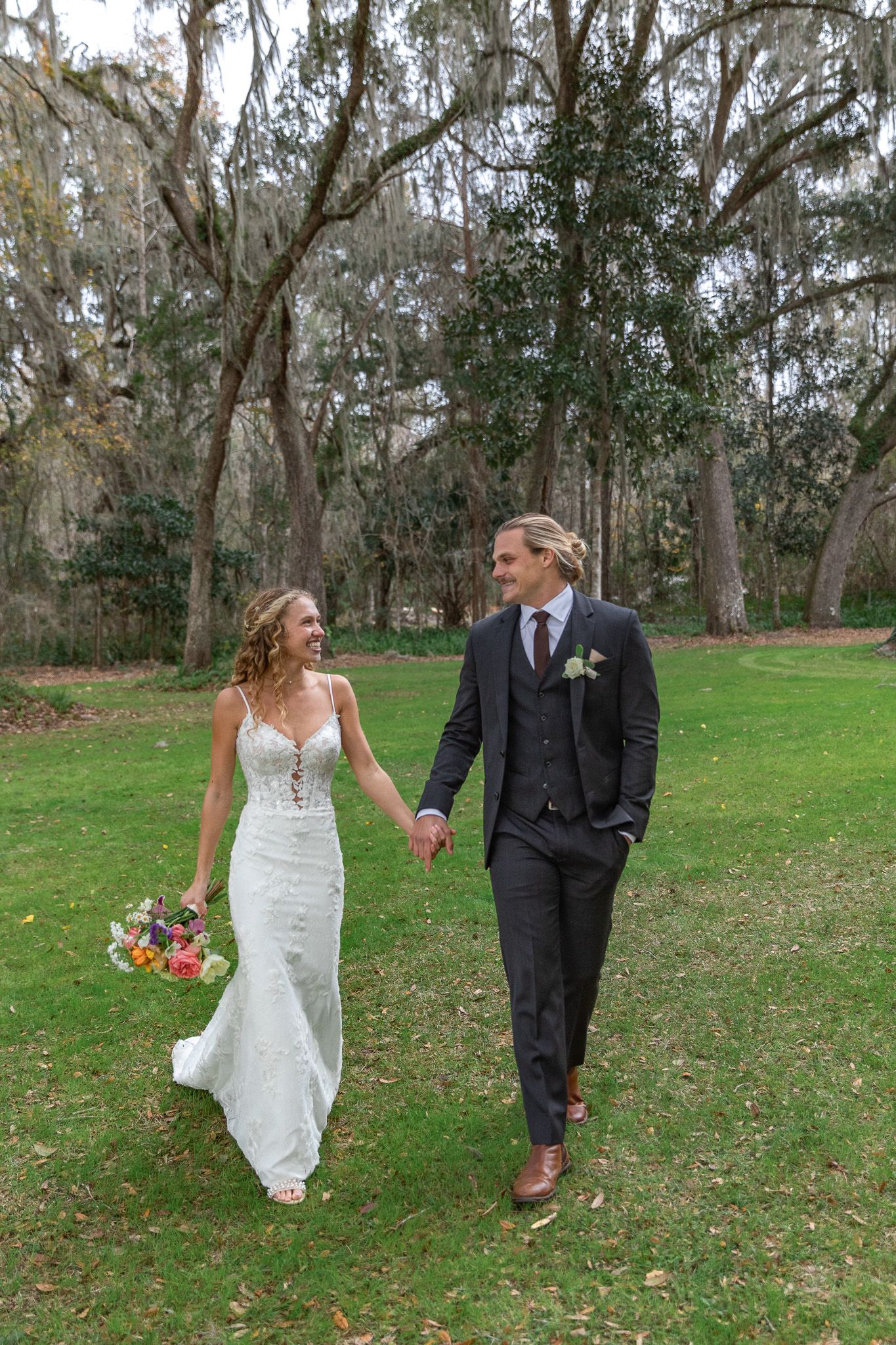 Orlando Luxury wedding photographer a couple in wedding attire walks together through a scenic outdoor park setting with grass and trees.