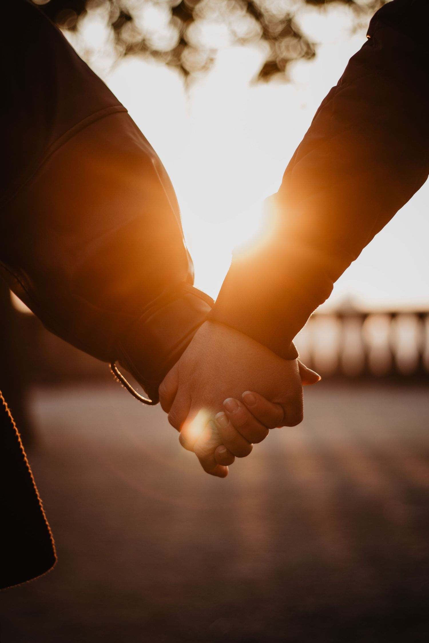 Photo à contre-jour d'un couple se tenant la main. Le soleil se reflète sur leurs mains.