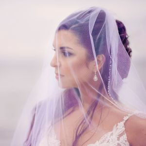 Elegant bride thoughtfully gazes into distance while covered by her veil