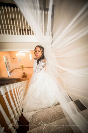 Bride blows kiss at camera while standing on large staircase and her veil trails behind her
