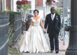 Bride and groom walk down sidewalk lined with red flowers and black iron fence