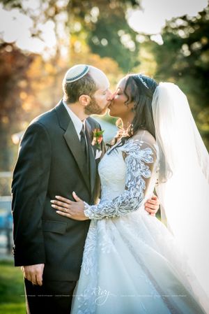 Jewish groom and black bride kiss with sunset in back