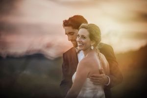 Bride laughs as groom holds her from behind with gorgeous sunset in back