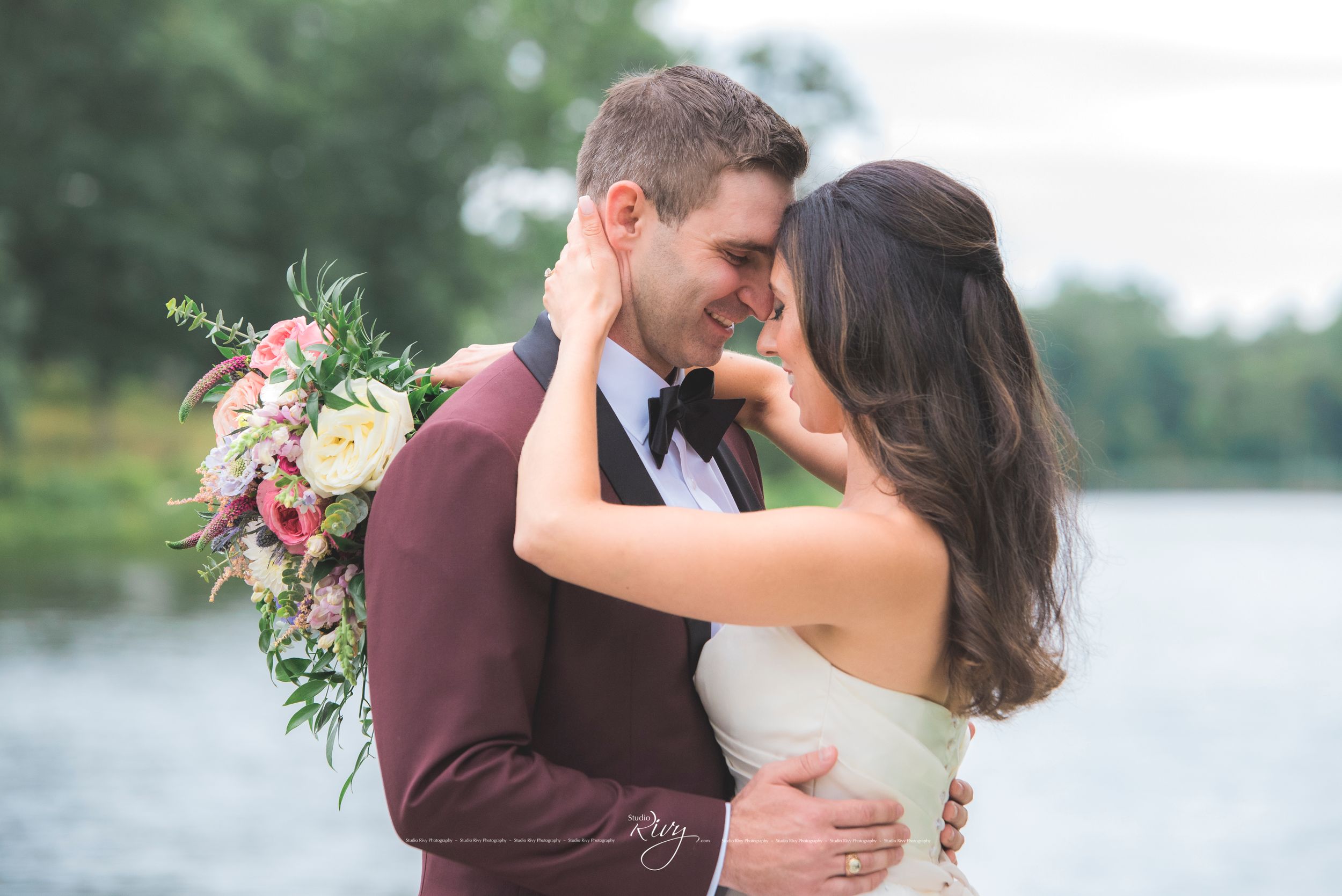 Bride and groom lean into embrace in front of vast lake