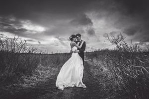 Black and white of bride and groom holding each other close with dramatic sky in back