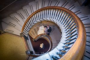 Bride and groom embrace at bottom of large spiral staircase