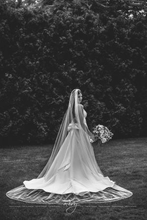 Elegant bride stands in wedding dress and veil with back to camera in black and white