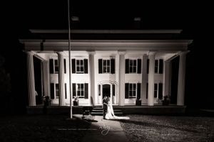 Bride and groom kiss near large white mansion