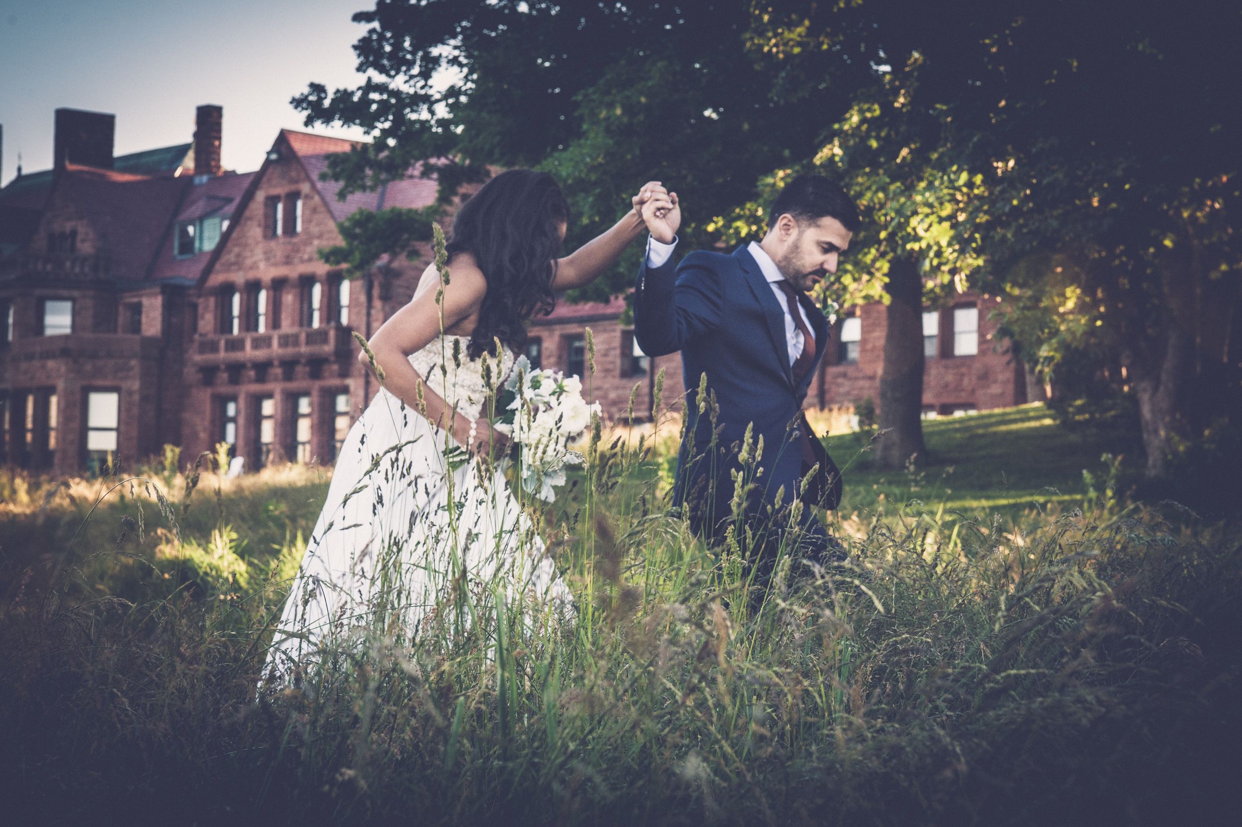 Groom leads his bride past a mansion and through a field