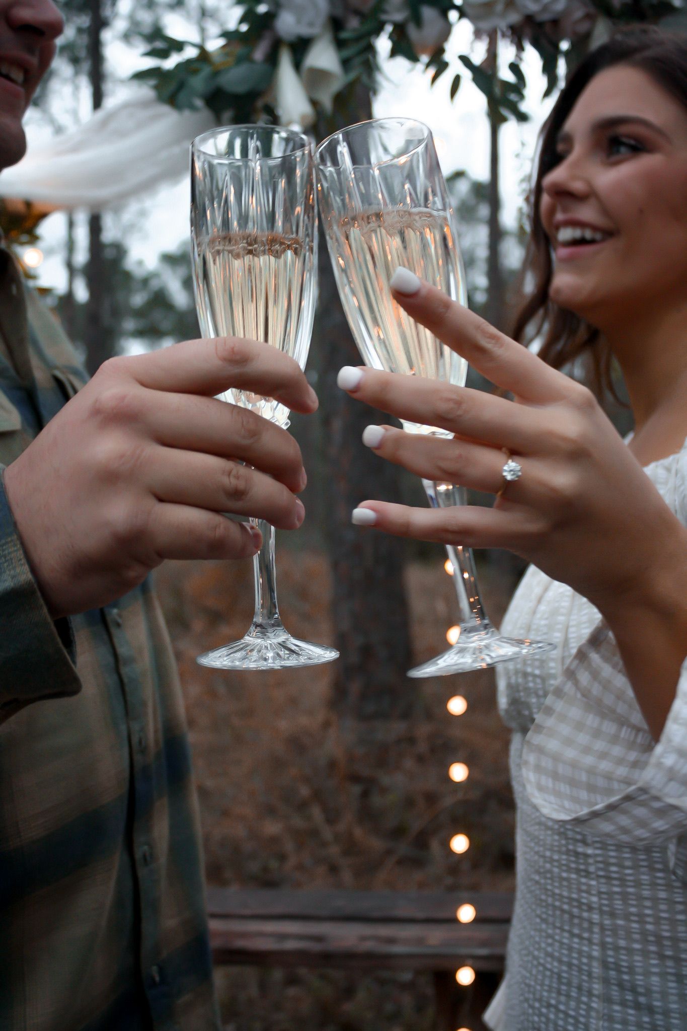 Two champagne flutes clink together in celebration with sparkly lights in background.