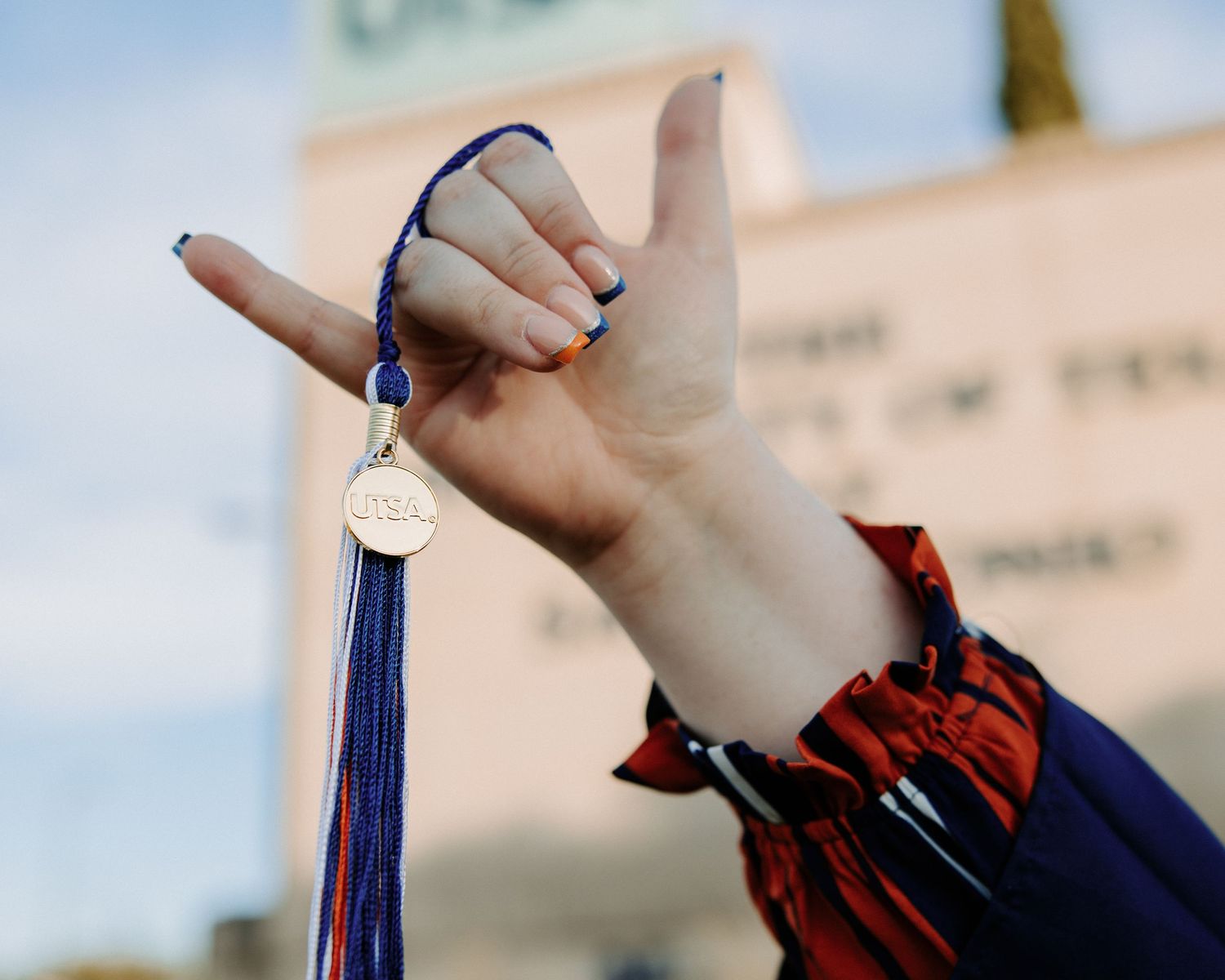 San Antonio Graduation. Hand holds up blue and gold graduation tassel against bright sky.