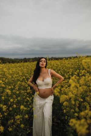 A peaceful maternity photo shoot in a blooming yellow canola field under moody overcast skies.