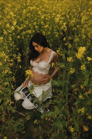 Intimate maternity photo in white lingerie among blooming yellow canola flowers in a golden field.