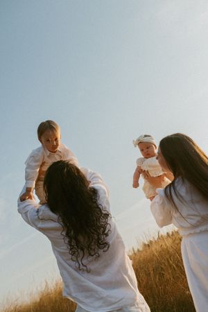 A group in white clothing plays together in a sunny field during golden hour.