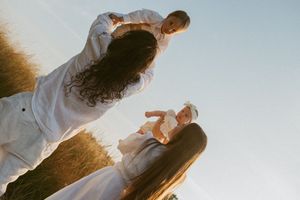 A couple in white clothing dance together in a field at sunset with golden light illuminating the scene.