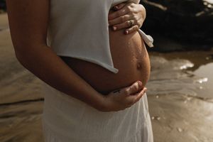 A pregnant person in a white dress gently cradles their bare belly in soft lighting.