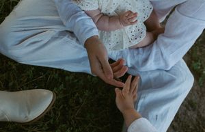 Two people wearing white clothing sit close together on grass while holding hands in an intimate moment.