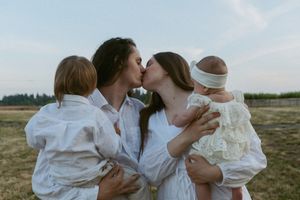 White-clothed figures sharing intimate embraces in a rustic outdoor field setting with natural lighting and pastoral scenery.