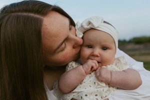 A tender moment captured as a parent kisses their baby's cheek outdoors during a photoshoot.