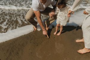 Bare feet standing on wet sand at the beach while writing or drawing in the sand during golden hour.