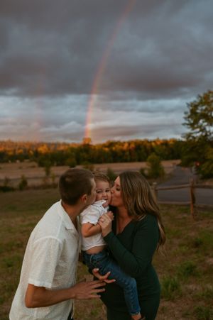 Family sharing an intimate moment outdoors with a rainbow in the background at sunset.