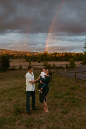 Family sharing a tender moment in a field at sunset with a beautiful double rainbow in the background.