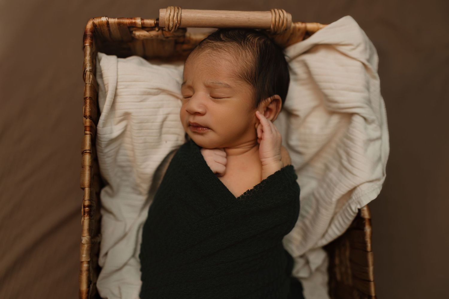 Peaceful sleeping newborn baby wrapped in black swaddle lying in rustic woven basket with white bedding. Colorado Springs Photographer.