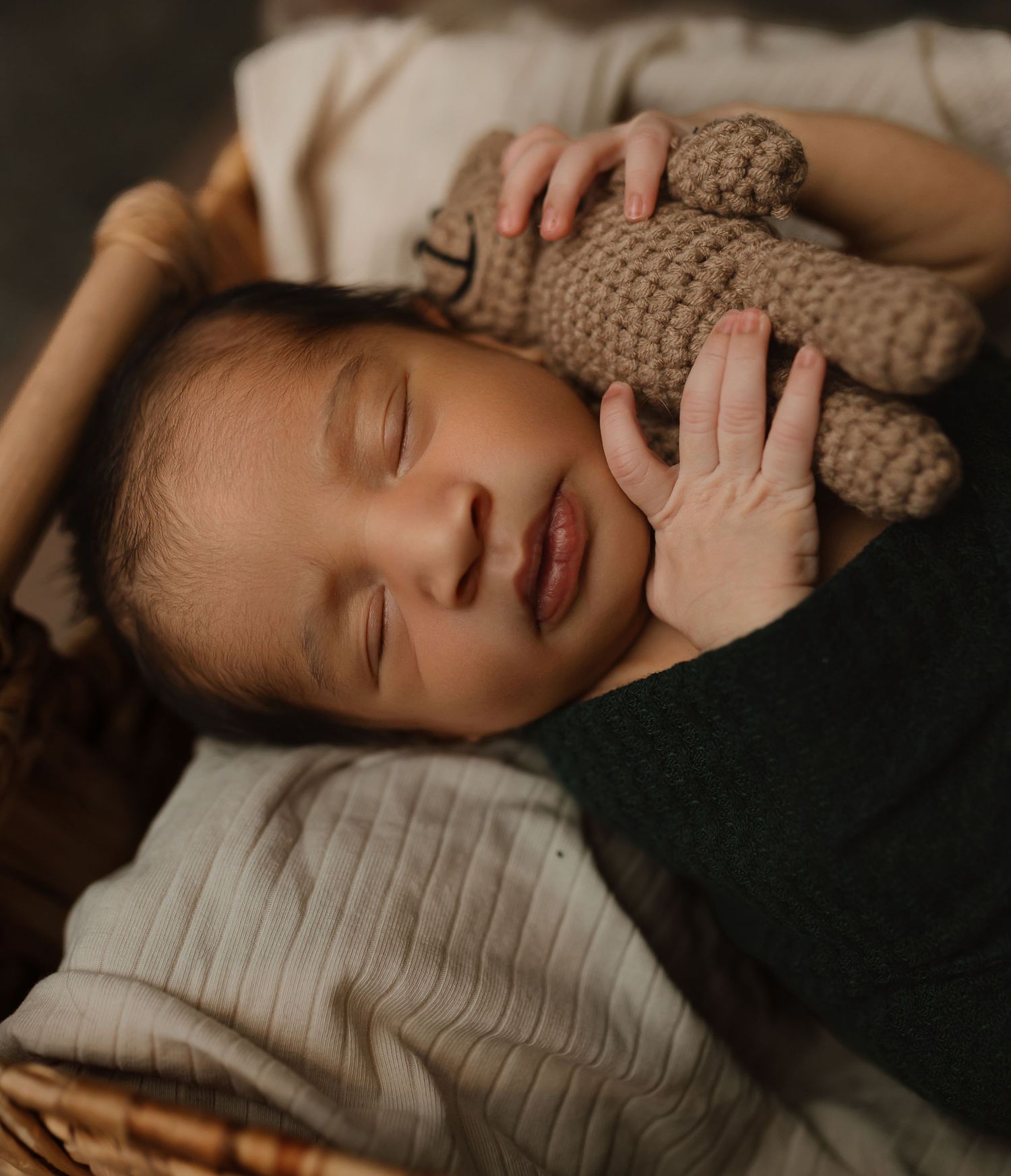 A sleeping infant cuddles a brown knitted stuffed animal toy while lying on soft bedding in warm lighting. Colorado Springs Photographer.