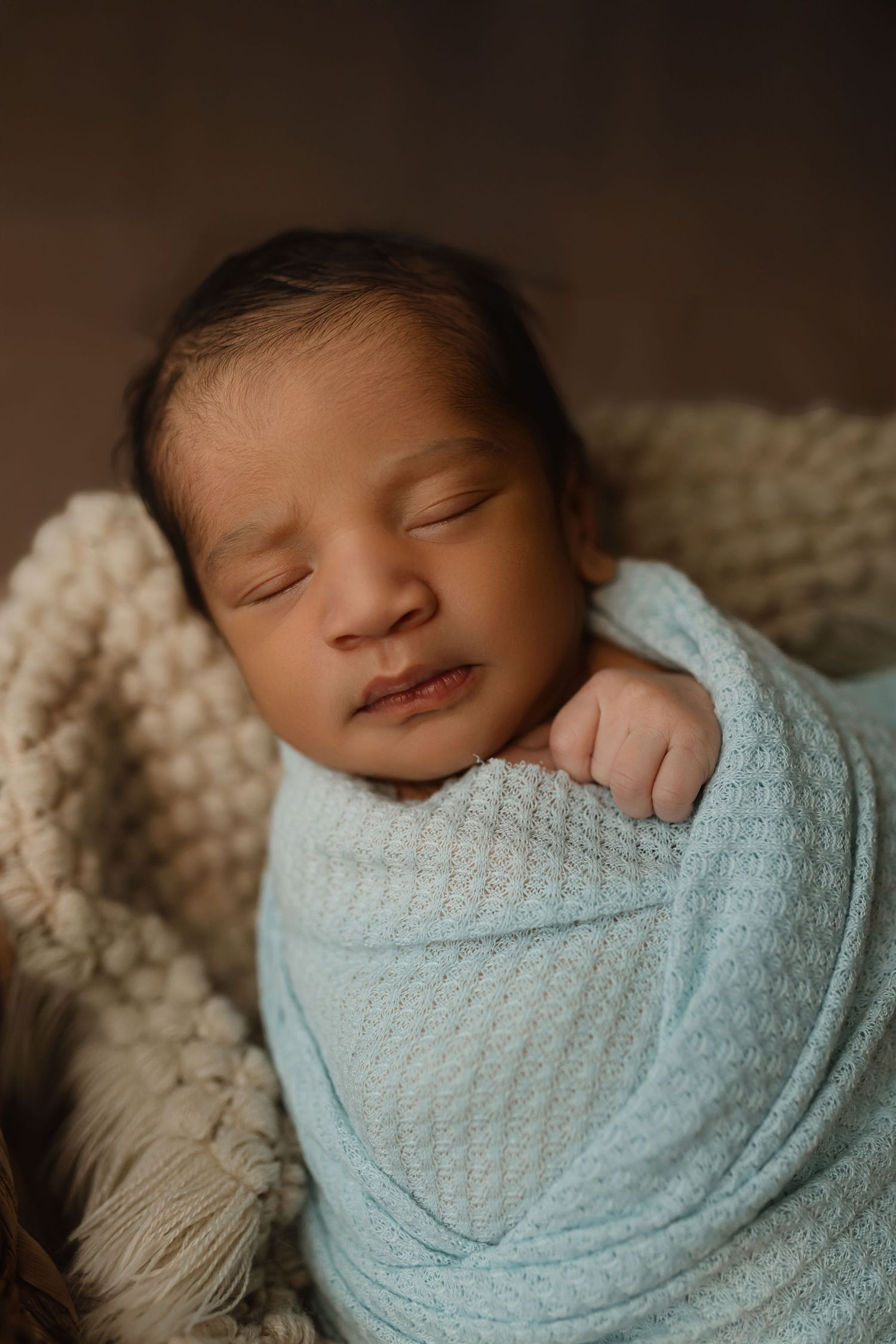 Peacefully sleeping newborn wrapped in soft blue swaddle blanket resting on cream knit blanket. Colorado Springs Photographer.