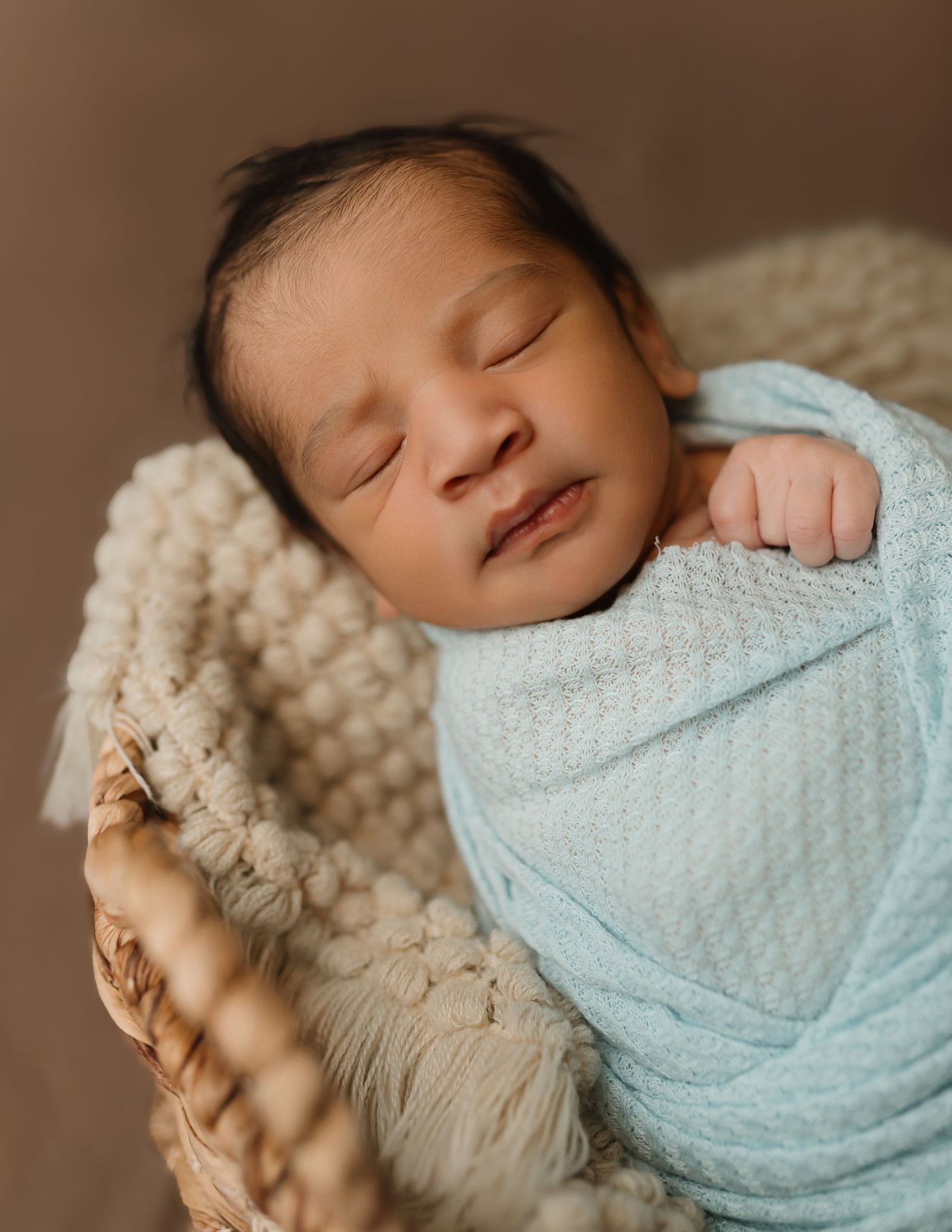 Sleeping newborn baby wrapped in light blue swaddle blanket rests peacefully on cream knit blanket. Colorado Springs Photographer.