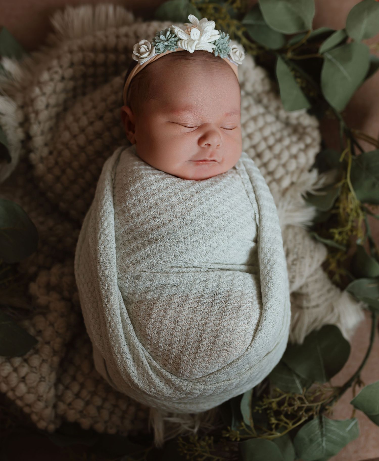 Sleeping infant in white wrap posed on knit blanket with greenery and floral crown decoration. Colorado Springs Photographer.