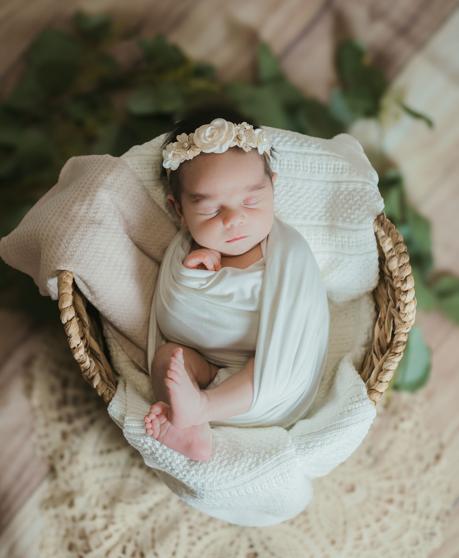 Sleeping newborn swaddled in white fabric lying in wicker basket with floral headpiece. Colorado Springs Photographer.