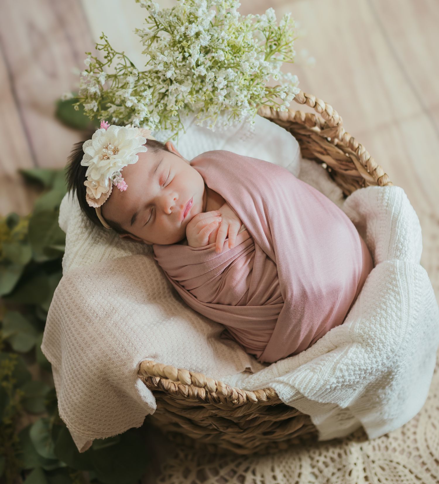 Sleeping baby wrapped in pink fabric with floral crown in cozy wicker basket. Colorado Springs Photographer.