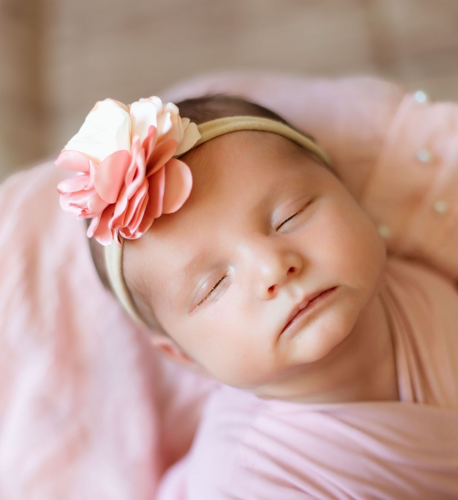 Sweet sleeping baby wrapped in soft pink blanket wearing a peach flower headband.