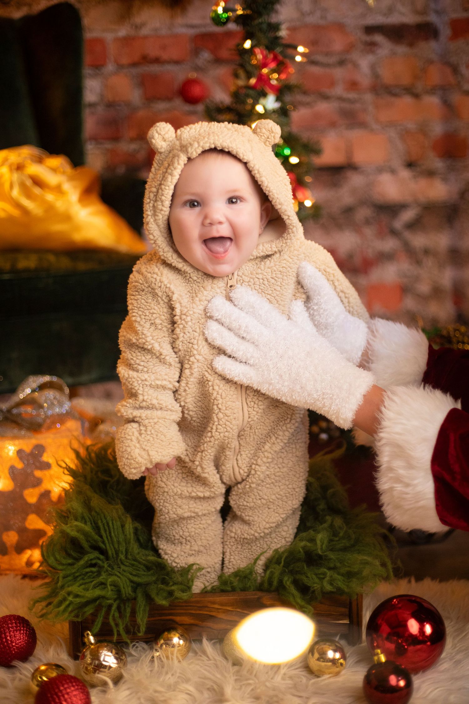 Baby in fluffy bear costume smiling near Christmas decorations and ornaments.