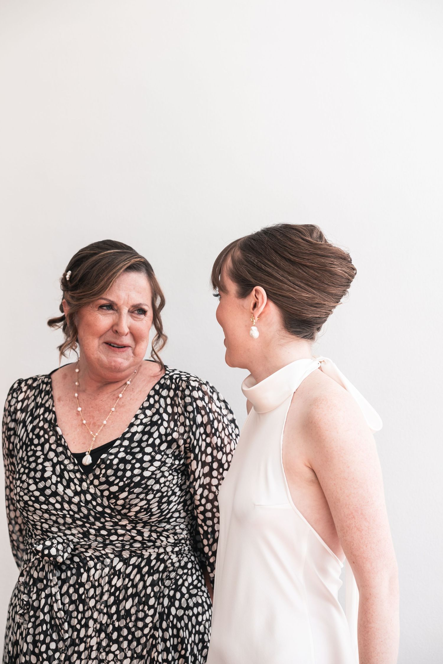 Two people share a tender moment while wearing formal attire against a white background.
