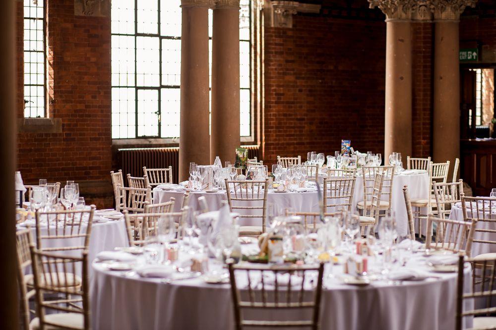 Elegant wedding reception venue with white chiavari chairs and round tables in a historic brick building.