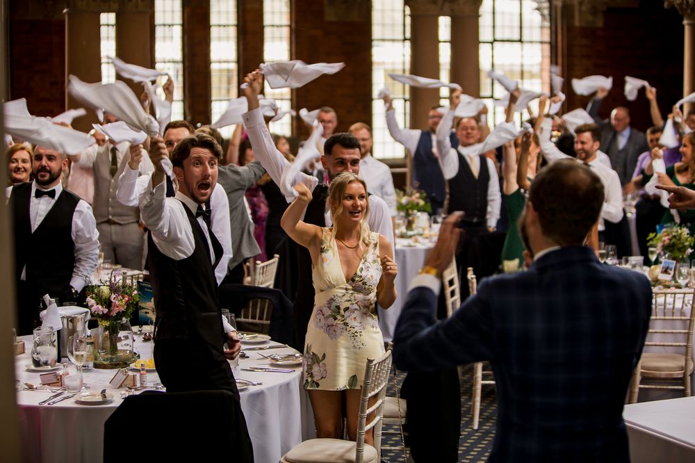 Wedding reception guests wave white napkins in celebration during a festive moment.