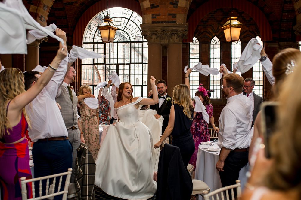 Wedding party and guests wave napkins in synchronized celebration during reception.