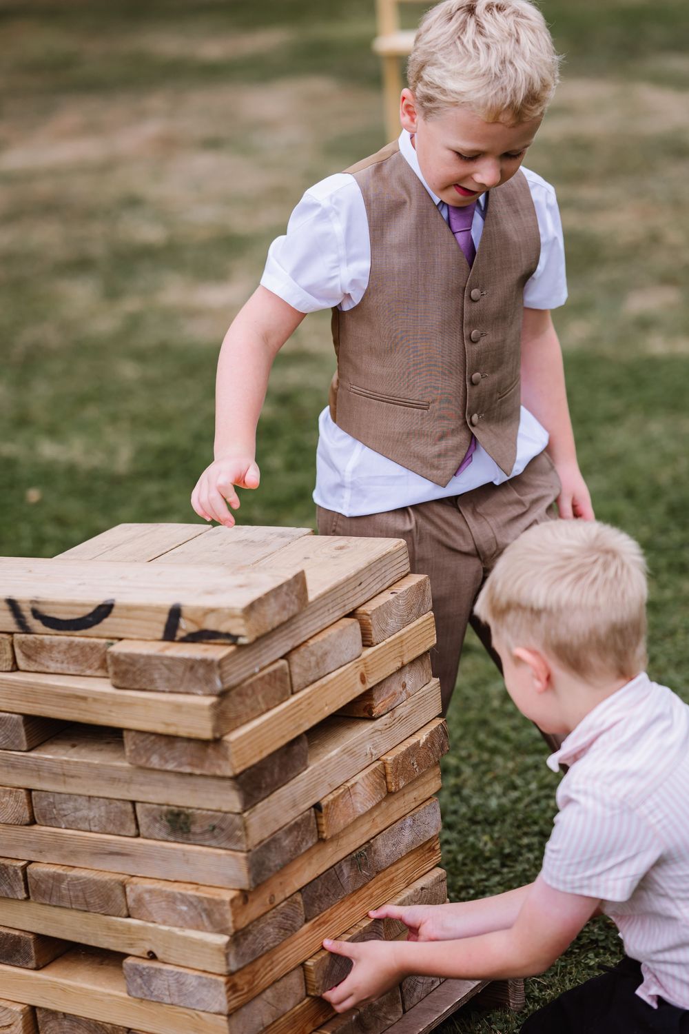 Children in formal attire playing with giant wooden Jenga blocks on grass during an a wedding at the Waterside Country barn and Mill a lakes