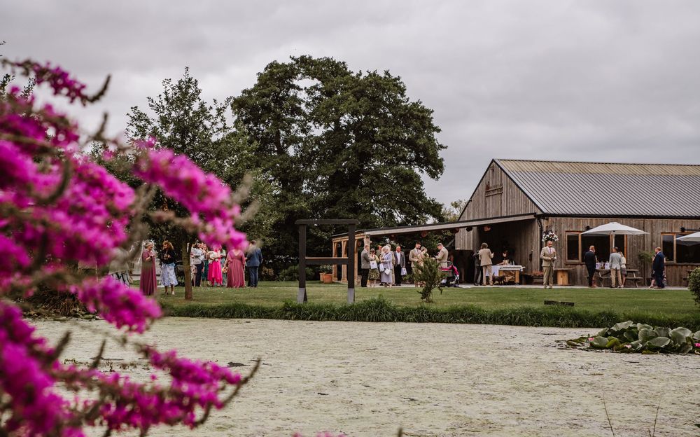 A rustic barn venue and outdoor ceremony space surrounded by blooming pink flowers and mature trees at the Waterside Country Barn and Mill